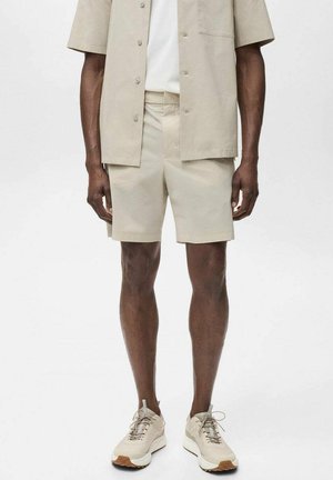 Chemise beige à manches courtes avec boutons et shorts assortis en tissu léger. Associée à des baskets aux tons neutres. Design simple, sans motifs.