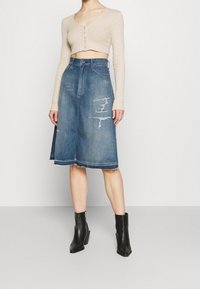 Denim midi kjol med slitna detaljer och fransad fåll, tillsammans med en beige kortärmad topp. Modellen bär svarta klackade ankelstövlar.