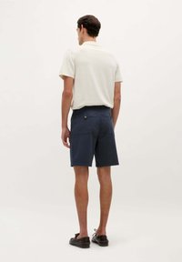 Chemise pour homme de couleur claire à manches courtes associée à un short navy. Le short dispose d'une poche arrière et d'une fermeture à bouton. Design simple, coupe décontractée.