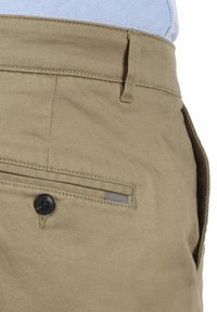 Pantalones de algodón beige con cierre de botón, bolsillos laterales y traseros, y un sutil detalle de tela a rayas en el bolsillo.