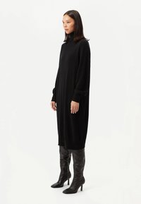 Svart stickad klänning med hög hals, långa ärmar och ribbade muddar. Kombinerad med svarta knähöga stövlar med klack.
