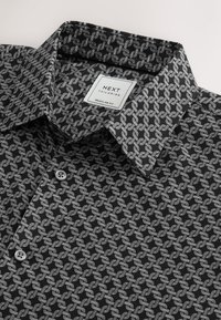 Camicia nera con motivo a nodo geometrico bianco, vestibilità regolare, con colletto classico e due bottoni grigi sulla patta.