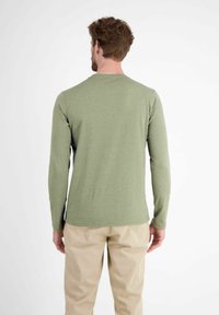 Langärmliges Shirt in Olivgrün, aus weichem Stoff. Runder Halsausschnitt und figurbetonter Schnitt. Kombiniert mit hellbeigen Hosen.
