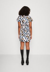 Robe à manches courtes avec un imprimé léopard multicolore sur un fond rose clair, cintrée à la taille, associée à des bottes noires jusqu'aux genoux.