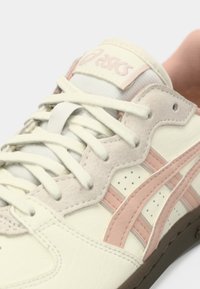 Baltos odinės sportbačiai su rožiniais akcentais, turintys tekstūruotą liežuvėlį, plokščias raišteles ir perforuotas šonines dalis; retro dizainas.