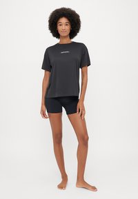 Maglietta nera a maniche corte con logo discreto sul petto, abbinata a pantaloni corti neri aderenti. Tessuto morbido, taglio rilassato, design minimalista.