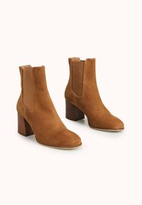 Bottines en daim marron avec panneaux latéraux élastiques, bout arrondi et talon moyen carré. Finition texturée avec une semelle lisse.