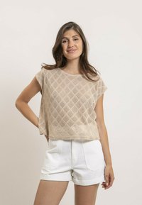 Haut beige à manches courtes avec un motif en tricot à losanges, associé à un short blanc taille haute. Texture lisse et coupe décontractée.