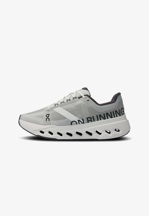 Adidași de alergare gri deschis cu brâu din plasă, șireturi plate, talpă cu amortizare și branding proeminent în negru pe lateral. Design elegant și modern.