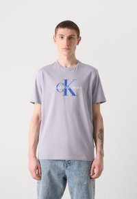 Light purple cotton t-shirt with a relaxed fit, featuring a blue "CK" logo and "Calvin Klein Jeans" text printed on the front.