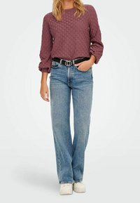 Bordeauxfarbener, strukturierten Pullover mit rundem Halsausschnitt, kombiniert mit hellblauen, geraden Jeans. Schwarzer Gürtel mit runder Schnalle und weißen Schuhen.