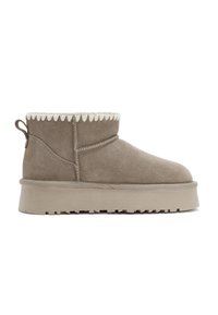 Taupe suède enkellaarsjes met een crème scalloped bovenkant, een stevige platformzool en een trekband aan de achterkant voor gemakkelijk aan- en uittrekken.