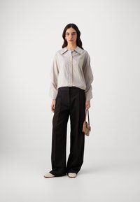 Cămășă cu dungi în albastru deschis și alb, asortată cu pantaloni negri cu talie înaltă. Adidași albi și o geantă mică completează ținuta.