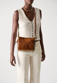 Brown suede crossbody bag with a quilted design, featuring a detachable strap and gold-tone hardware. Textured surface with solid accents.