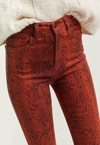 Rode jeans met een slangenhuidpatroon, slim fit, met zijzakken en een knoopsluiting. Gestructureerd oppervlak met een lichte glans.