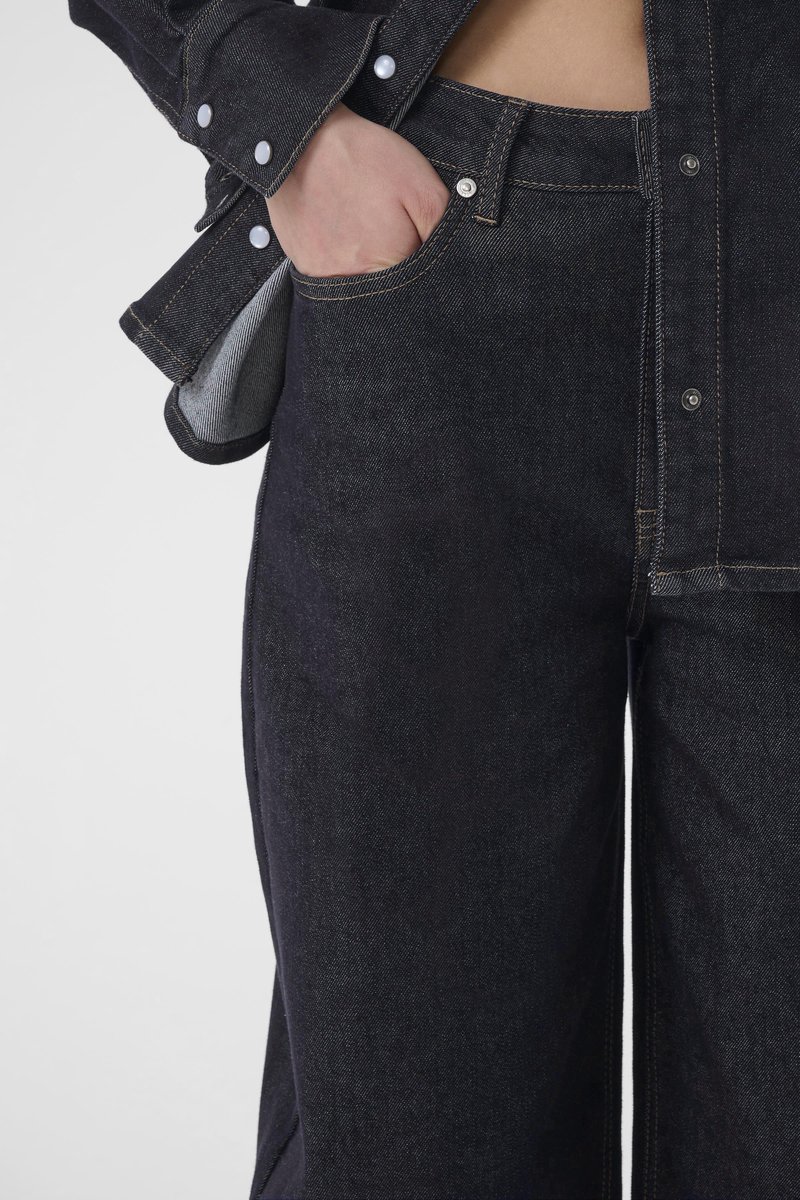Dark denim fabric, straight-leg jeans with a top button and front pockets. Closely fitted shirt with snap buttons and contrasting inner fabric.