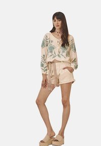 Blusa beige con bordado floral verde, combinada con pantalones cortos beige claros que cuentan con un cinturón atado. Sandalias de plataforma completan el conjunto.