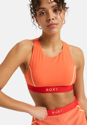 Orange athletic crop top with a round neckline, featuring a red band labeled "ROXY" and light-colored accents along the seams.