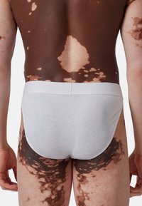 Slip in cotone bianco con design senza cuciture. Pelle con un motivo patchwork marrone e chiaro visibile sulla schiena e sulle cosce.