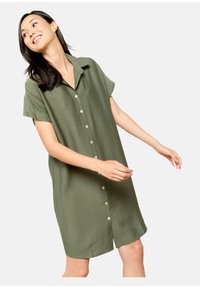 Sukienka koszulowa z krótkim rękawem w oliwkowym kolorze, z zapięciem na guziki z przodu i luźnym krojem. Posiada kołnierzyk oraz miękką teksturę.
