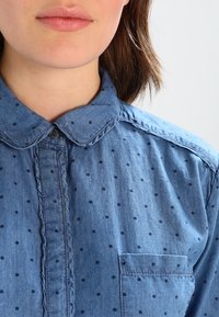 Ljusblå denimskjorta med knappad krage, som har ett svagt prickigt mönster och en bröstficka på vänster sida. Mjukt material och avslappnad design.