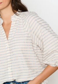 Lätt, knappupp-blus med ett mjukt rosa- och blårutigt mönster, med en volangkrage och något pösiga ärmar.