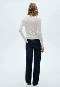 Un haut à manches longues côtelé beige clair associé à un jean large bleu foncé. Le haut présente une silhouette ajustée, tandis que le jean possède des poches classiques.