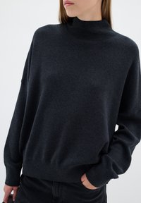 Mörkgrå, höghalssweater i mjukt stickat material; har en avslappnad passform, sänkta axlar och ribbade muddar och nederkant.