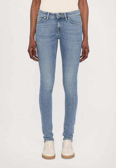 Jean skinny bleu clair en denim, avec un design classique à cinq poches, un léger effet de décoloration, et une taille mi-haute, associés à des baskets blanches.