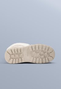 Buty sportowe z teksturowaną białą cholewką, kremową gumową podeszwą i wzorzystym bieżnikiem. Na podeszwie znajduje się logo, a przód buta ma zaokrąglony kształt.