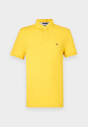 Dzeltena kokvilnas polo krekls ar klasisku apkakli, īsām piedurknēm un mazu logotipu uz krūšu. Gluda struktūra un regulāra piegriezuma.