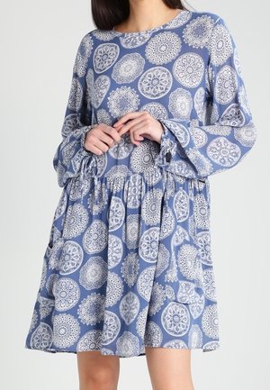 Blå mønstret kjole lavet af letvægtsstof. Har lange ærmer, en rynket talje og et udvidet skørt med indviklede hvide mønstre.