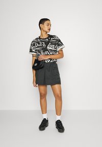 Black and white graphic T-shirt with bold text, paired with a dark pleated skirt, black crossbody bag, and chunky black sneakers.