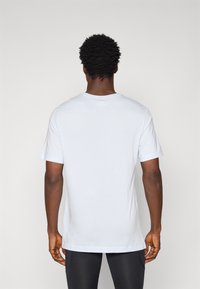 Bílé bavlněné tričko s kulatým výstřihem, krátkými rukávy a volným střihem, s hladkou texturou bez viditelných vzorů nebo kovových doplňků.