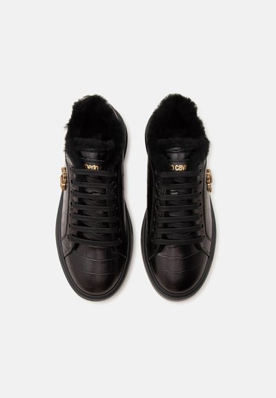 Paire de baskets en cuir noir avec texture crocodile, lacets noirs, doublure en fourrure et boucle décorative dorée sur le côté.
