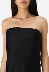 Melnas strapless top, kas veidots ar gludu, viendabīgu tekstūru. Audums izskatās viegls ar maigu spīdumu, veidojot taisnu piegriezumu.