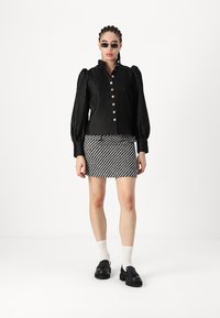 Black pleated blouse with puffed sleeves and silver buttons, paired with a striped black and white mini skirt and chunky black shoes.