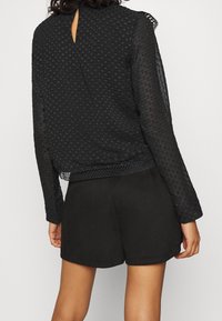 Musta tekstuuriga bluus pikkade varrukatega, tagaküljel võtmepesa avamine ja pitsääris, koos mustade lühikeste pükste paariga.