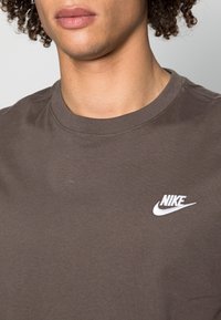 Brun bomulls t-shirt med rund hals och korta ärmar. Har en vit broderad Nike-logotyp på vänster bröst. Mjuk textur.