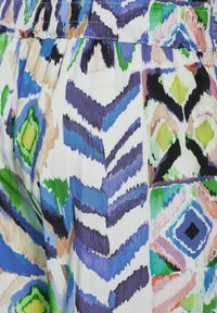 Tessuto multicolore con motivi astratti a zigzag e a diamante. I colori predominanti includono blu, verde e nero su uno sfondo bianco.