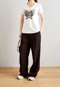 Vit kortärmad t-shirt med fjärilsgrafik, ihop med svarta vida byxor och silversneakers. Tillbehören inkluderar en liten svart väska.