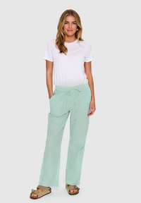 T-shirt à col rond blanc, pantalon léger à rayures vertes décontracté avec une taille élastique, poches latérales, et sandales plates avec un accent en nœud.