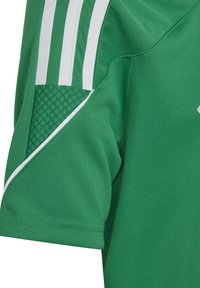 Maglia sportiva verde realizzata in tessuto traspirante, con strisce bianche decorative sulle spalle e un pannello testurizzato sulle spalle.