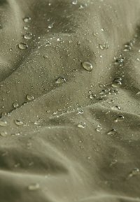 Gouttes d'eau perlées sur un tissu imperméable vert olive, montrant la texture et la résistance à l'eau.