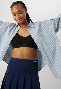 Lyseblå stribede oversized skjorte, sort sportsbh og navy plisseret nederdel. Funktioner inkluderer knaplukning og logo-beklædt talje.