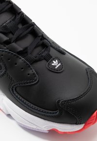 Black leather sneaker with textured surface, featuring black laces, white logo patch, and a contrasting white and red sole.