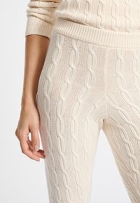 Beige kabelgebreide sweater broek met een geribde tailleband, een textuurpatroon van in elkaar geweven lussen en een strakke pasvorm bij de enkel.