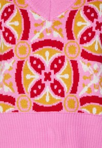 Stickad tröja med en rosa kropp och ett färgglatt geometriskt mönster i röd, gul och vit vid halsringningen och övre delen.