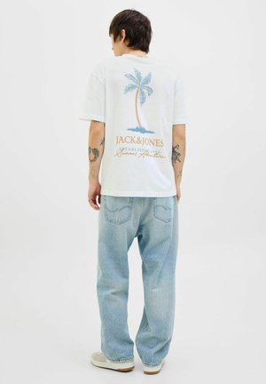 Lysfarvet bomulds t-shirt med et palmetræ grafik og tekst på ryggen, parret med løstsiddende lyseblå denim jeans.