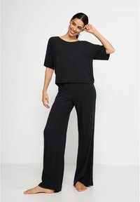 Fekete loungewear szett, amely egy lazán illeszkedő, rövid ujjú felsőből és széles szárú nadrágból áll, puha, könnyű anyagból, sima textúrával.